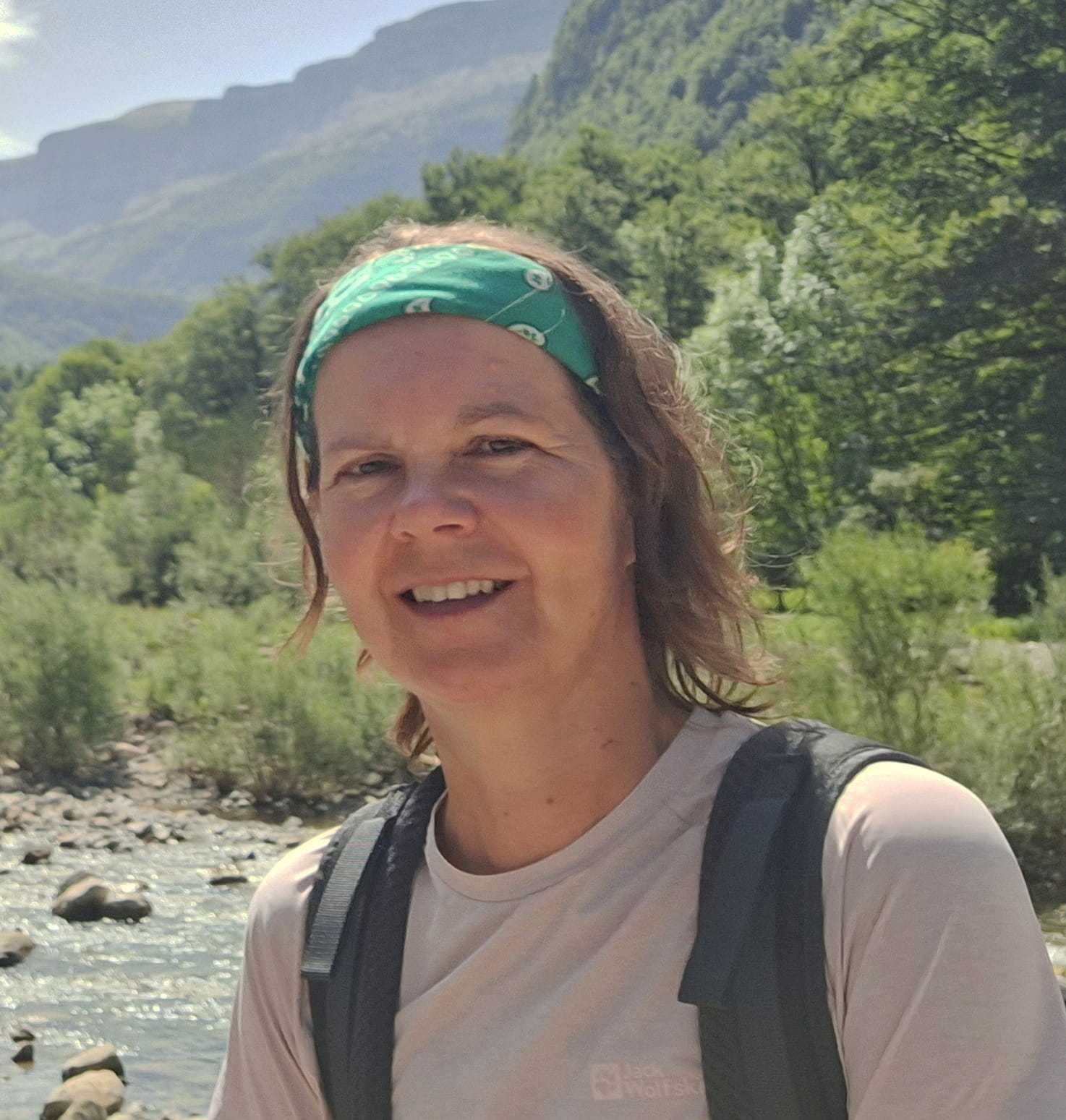 Esther met wandelrugzak bij een rivier, met bergen op de achtergrond